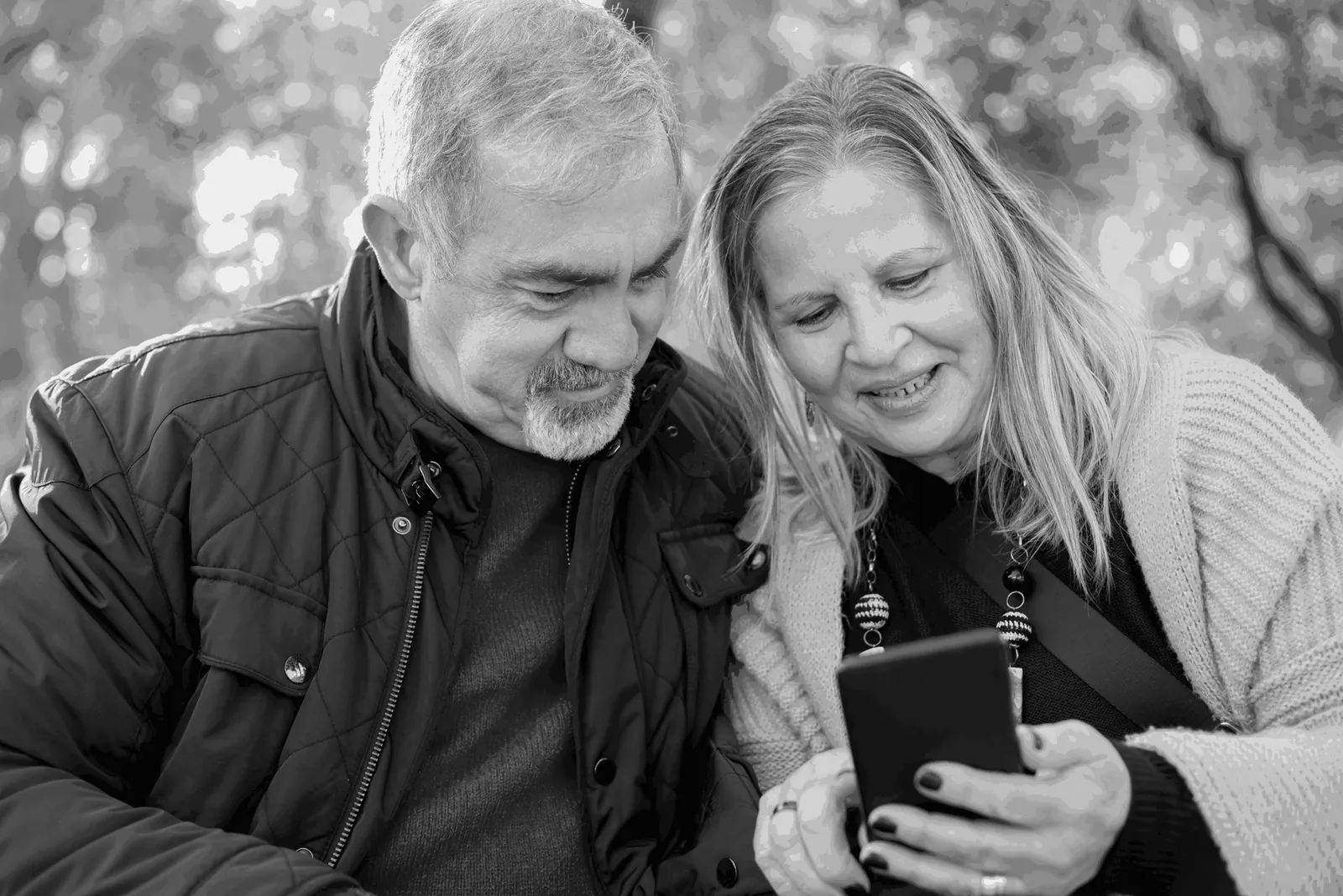An older couple reading a phone together outdoors